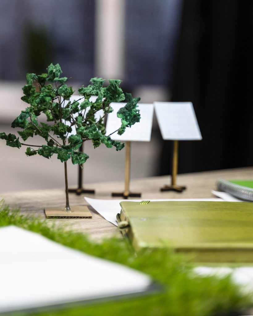 Duurzaam bouwen: maquette met mini-zonnepanelen en boom op ontwerptafel — relevant bij SEO-teksten laten schrijven.